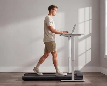 Man walking on a Movaped compact walking pad treadmill while working at a standing desk